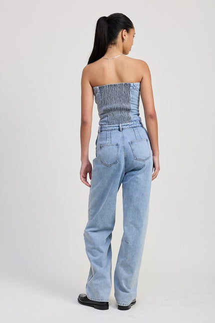 Back view of a light-wash strapless denim jumpsuit featuring a smocked elastic back panel, fitted bodice, and wide-leg pants with patch pockets.