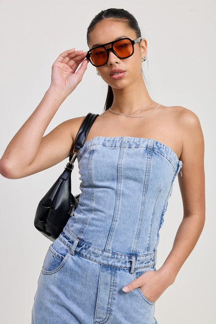 A close-up view of a strapless denim jumpsuit, highlighting its structured seam details and fitted bodice. The light-wash denim fabric has a slightly faded look, giving it a modern yet casual style.