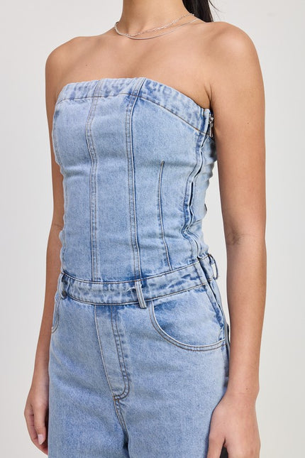 A close-up of a strapless denim jumpsuit, showcasing its structured bodice with vertical seam details and a side zipper. The light-wash denim fabric features a fitted waistline with belt loops and front pockets, giving a stylish yet casual look.